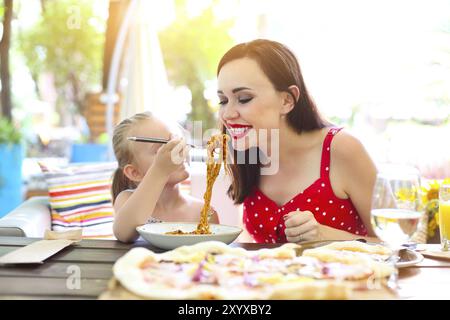 Glückliche Mutter und Tochter essen spaghetti bolognese im Restaurant zusammen Stockfoto