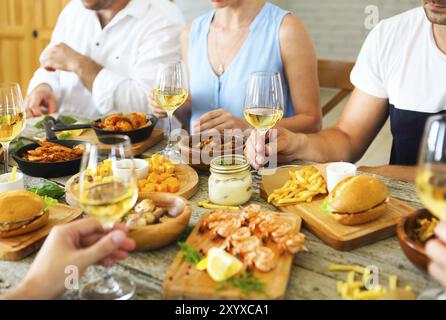 Hände mit weißen Wein Toasten über serviert Tisch mit Essen. Freundschaft und Glück Konzept Stockfoto