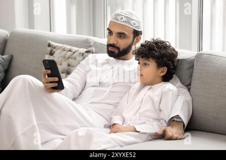 Seriöser arabischer Vater und neugieriger süßer kleiner Sohn mit Anwendung Stockfoto