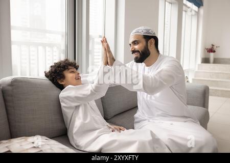 Glücklicher muslimischer Vater, der dem fröhlichen kleinen Sohn hohe fünf schenkt Stockfoto