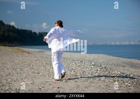 Eine Frau in weißen Kleidern läuft an einem windigen Kiesstrand entlang. Stockfoto