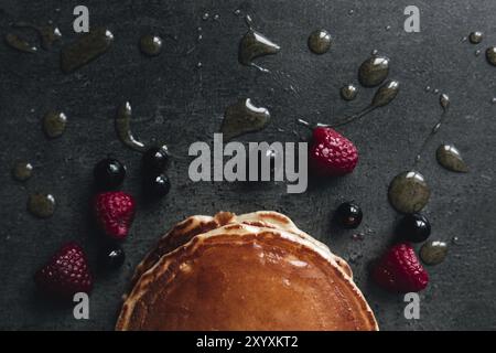 Saftige Pfannkuchen mit Beeren, Honig, Löffel auf einem schwarz-grauen Betontisch. Stockfoto