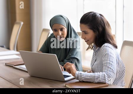 Zwei junge arabische und hispanische Managerinnen arbeiten am Laptop Stockfoto