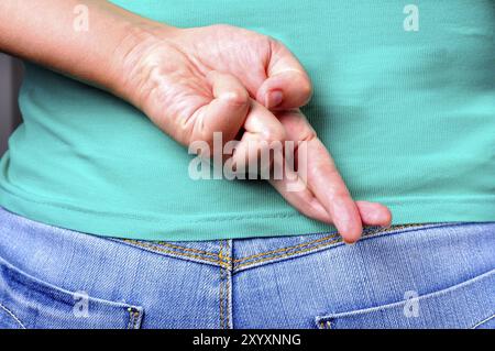 Nahaufnahme von gekreuzten Fingern hinter einer Frau Rücken Stockfoto