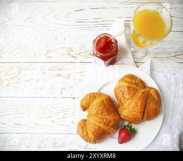 Zwei leckere Croissants auf dem Teller und Erdbeermarmelade auf hölzernen Hintergrund. Ansicht von oben Stockfoto