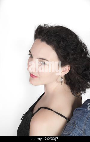 Junge Modell in ihrer Mitte der 20er Jahre sitzt auf einem Stuhl mit einer blauen Jeans Jacke hängt über der Stuhllehne Stockfoto