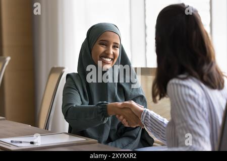 Glückliche, schöne arabische Geschäftsfrau, die der Kollegin die Hand schüttelt Stockfoto