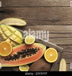 Frische tropische Früchte in einem Holzlieferkarton auf einem Holzhintergrund. Papaya, Orange, Banane, Kokosnuss, Mango und Zitrone Draufsicht flach mit Kopie sp Stockfoto