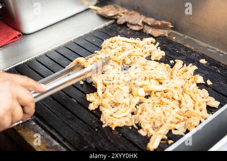 Eine Person kocht Antikuchos auf einem Grill. Das Fleisch wird auf Spießen gekocht und wird von anderem Fleisch umgeben Stockfoto