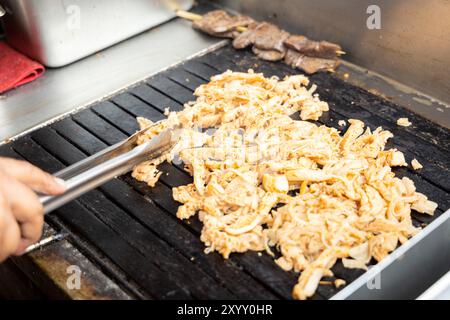 Eine Person kocht Antikuchos auf einem Grill. Das Fleisch wird auf Spießen gekocht und wird von anderem Fleisch umgeben Stockfoto