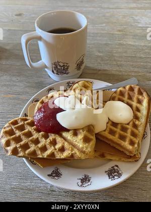 Waffeln mit Marmelade, Sahne und Käse auf einem Teller, neben einer Tasse Kaffee, serviert auf einem Holztisch, norwegisches Nationalgericht, Roeros, Norwegen, Europa Stockfoto