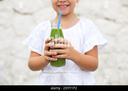 Kleine Mädchen trinken grünen frischen Saft mit Stroh im Freien. Nahaufnahme Stockfoto