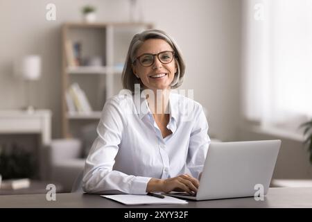 Glückliche Frau mittleren Alters sitzt im Home Office mit Laptop Stockfoto