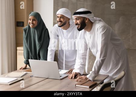 Fröhliche junge Geschäftskollegen aus dem Nahen Osten, die am Meeting-Tisch stehen Stockfoto