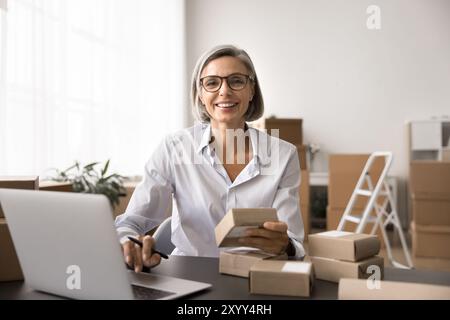 Porträt einer Reifen Frau, die am Arbeitsplatz sitzt und von Kästen umgeben ist Stockfoto