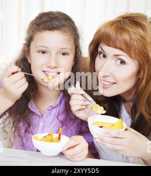 Glückliche Mutter und Tochter essen Müsli und Obst Stockfoto