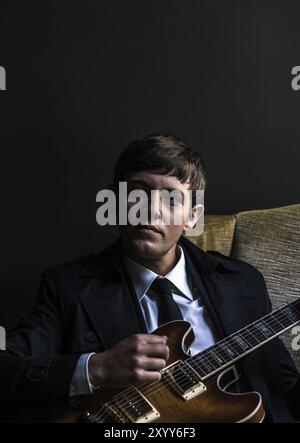 Ein junger Mann im Anzug setzt sich hin und spielt Gitarre Stockfoto