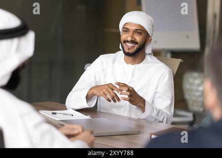 Glücklicher, gutaussehender junger arabischer Geschäftsmann, der mit verschiedenen Kollegen spricht Stockfoto
