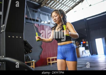 Tiefwinkelansicht einer starken chinesischen jungen Frau, die Gewichte mit dem lat-Rudergerät im Fitnessstudio zieht Stockfoto