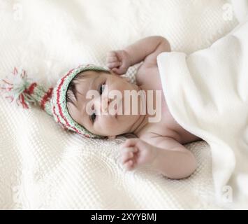 Porträt eines Babys in Strickmütze, das auf dem Bett liegt. Einen Monat alt Stockfoto