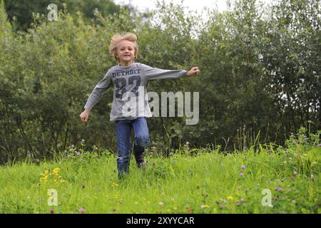 Kleiner Junge, der draußen auf einer Wiese läuft. Blonder Junge, der über eine Wiese läuft Stockfoto