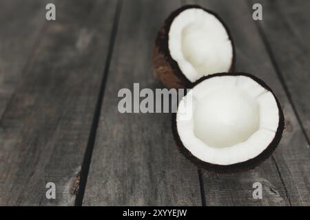 Gebrochene Kokosnüsse auf grauem hölzernem Hintergrund. Weißes Kokosnussfleisch. Stockfoto