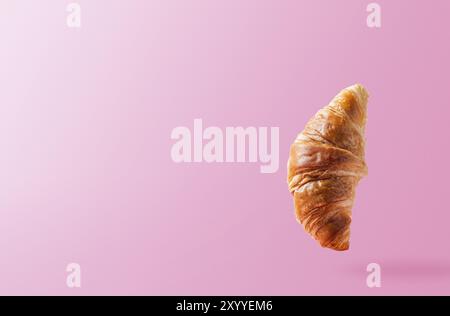 Frisch gebackene Croissants schweben oder fliegen. Croissant fliegen in der Luft isoliert auf rosa Hintergrund. Levitation-Szene. Platz kopieren. Schild im Scheinlook Stockfoto