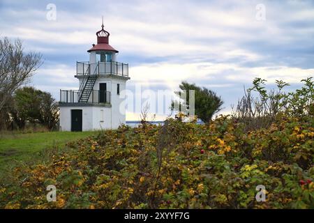 Leuchtturm, Spodsbjerg Fyr in Huntsted an der Küste Dänemarks. Die Sonne scheint durch die Wolken. Wiese mit Bäumen. Landschaftsfoto vom Meer Stockfoto