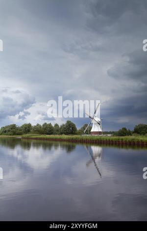 Windmühle am Fluss über bewölktem stürmischem Himmel, Niederlande Stockfoto