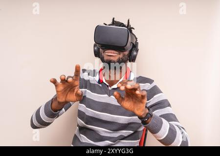 Junger afroamerikanischer Mann mit VR-Headset und Kopfhörern, Gesten mit Händen. Konzept von Virtual-Reality-Technologie, Gaming und immersiver Ziffer Stockfoto