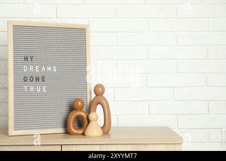 Brieftafel mit dem Satz My Dreams Come True und Dekorationselementen auf einem hölzernen Beistelltisch in der Nähe einer weißen Ziegelwand, Platz für Text Stockfoto