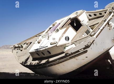 Die alte Yacht liegt auf dem Sand in der Wüste vor dem blauen Himmel Stockfoto