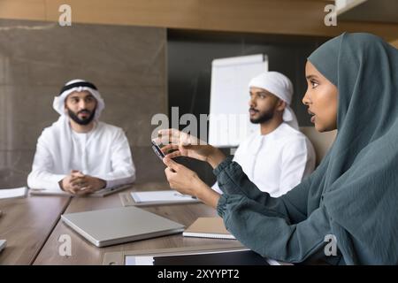 Ernsthafte, schöne arabische Geschäftsfrau im Hijab, die mit männlichen Kollegen spricht Stockfoto