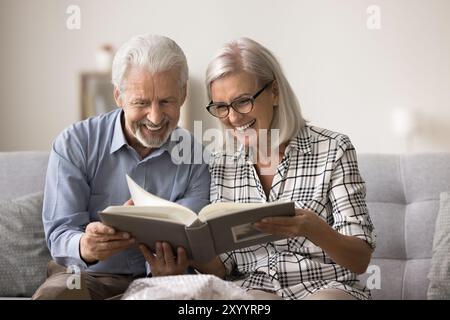 Seniorenpaar, das sich in einem Fotoalbum die schönsten Momente des Familienlebens ansieht Stockfoto