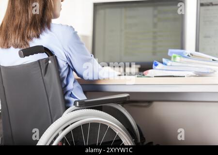 Ungültige oder behinderte junge geschäftsfrau sitzende Person Rollstuhl arbeiten Büro Schreibtisch computer Stockfoto