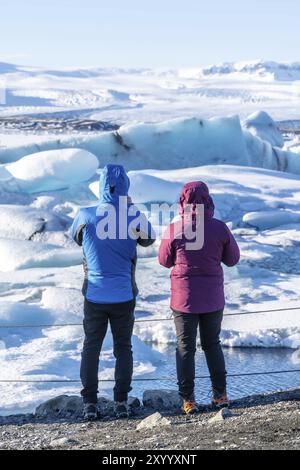 Ein paar Touristen, die schwimmende Eisberge in der Gletscherlagune Jokulsarlon in Island beobachten Stockfoto