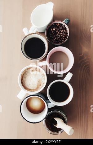 Mehrere Kaffeetassen und bunte Tassen mit Americano, Espresso, Latte und Cappuccino, Milchglas, geröstete Kaffeebohnen in Glasflasche, Holzlöffel Stockfoto