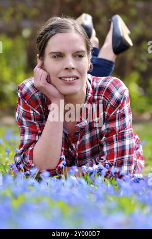 Schöne junge Frau, die im Frühjahr auf einer Wiese mit blühendem Blauchen (scilla bifolia) liegt und das warme Sonnenlicht genießt Young attraktive Woma Stockfoto