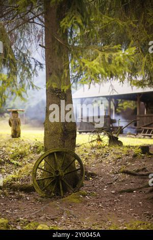 Ein altes Wagenrad auf einem Baumstamm vor einer Hütte aus Holzrauch dringt ein, ein altes Wagenrad auf einem Baumstamm vor einer Hütte aus Holz s Stockfoto