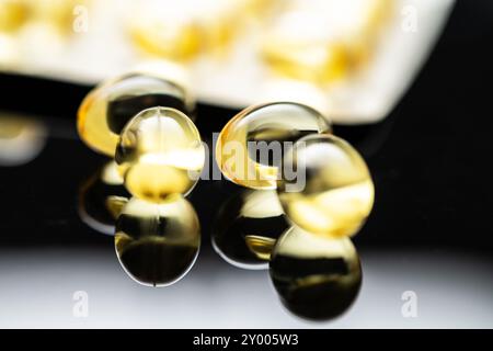 Gelbe durchscheinende Kapseln mit Vitamin D und Omega-3-Fischöl. Kapseln auf einer reflektierenden Oberfläche und Blisterpackung zur Förderung der Heilung Stockfoto