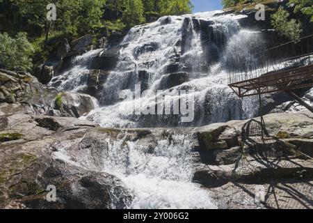 Ein großer Wasserfall fließt über Felsen mit einer Attika im Vordergrund, umgeben von Bäumen an einem klaren Tag, Cascada del Caozo, Garganta de Bonal de los L Stockfoto