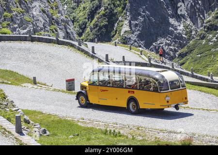 Der historische postbus fährt entlang der Tremola, der weltberühmten Serpentinenstraße durch das Val Tremolo. Touristenbus auf der Tremola-Straße, Schweiz Stockfoto