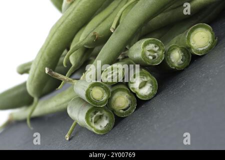 Ein Haufen geschnittener grüner Bohnen auf einem Tisch aus schwarzem Stein auf weißem Hintergrund. Bio- und Diätkost Stockfoto