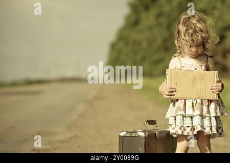 Einsames Mädchen mit Koffer, der auf der Straße steht und Papier hält, mit Copyspace in den Händen Stockfoto