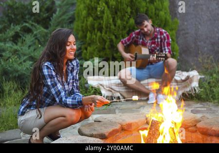 Junges Paar mit Gitarre in der Nähe von Feuer im Freien. Reisen und Ferien Konzept Stockfoto