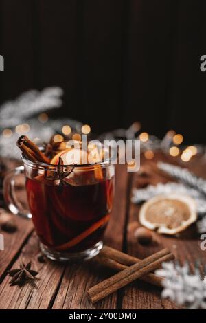 Weihnachtszeit Konzeptfoto. Glasbecher oder Becher mit Glühwein innen auf Holztisch, Hintergrund. Girlanden, Weihnachtsschmuck, Zimt, Haselnu Stockfoto