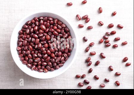 Adzuki-Bohnen in einer weißen Schüssel auf Leinenstoff. Auch bekannt als Azuki, Aduki, rote oder rote Mungbohne. Getrocknete Samen von Vigna angularis. Stockfoto