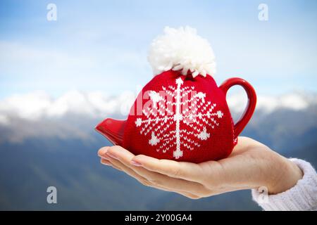 Teekanne in der geknoteten Kappe in der Hand einer Frau vor Bergkulisse Stockfoto