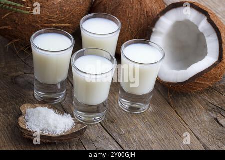 Kokosmilch im Glas mit Kokosnussschalen auf altem hölzernem Hintergrund, selektiver Fokus Stockfoto