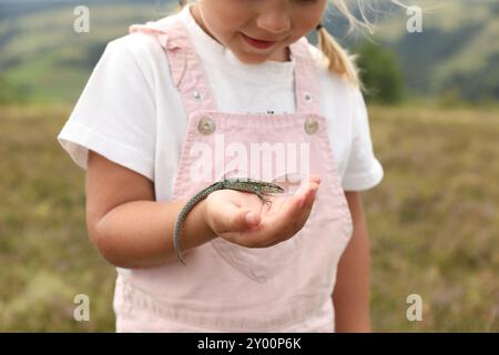 Kleines Mädchen mit Eidechse auf verschwommenem Hintergrund, Nahaufnahme. Kind genießt wunderschöne Natur Stockfoto